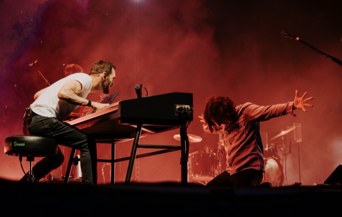 Johnny McDaid leaning into the keys beside a bandmate kneeling in red stage haze