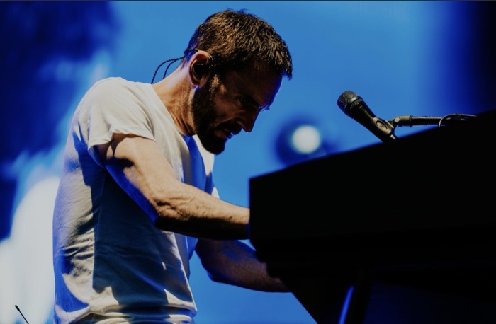 Johnny McDaid with head bowed over the keyboard in blue light