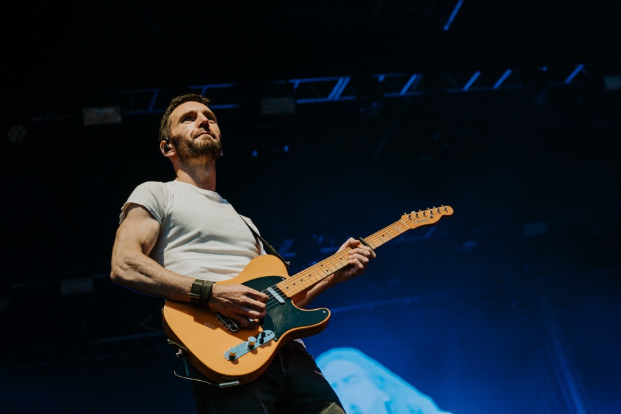 Johnny McDaid playing a Telecaster beneath blue stage rigging