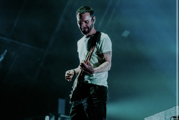 Johnny McDaid smiling while playing guitar in teal light